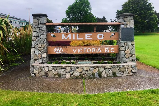 Un cartel de piedra y madera con el texto Mile 0 Victoria B.C. sobre el césped