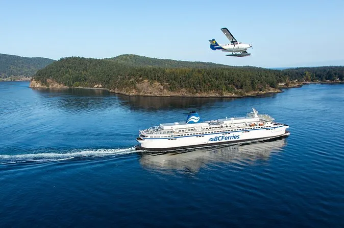 Un navire BC Ferries traversant l'eau libre près d'une île boisée pendant qu'un hydravion vole au-dessus